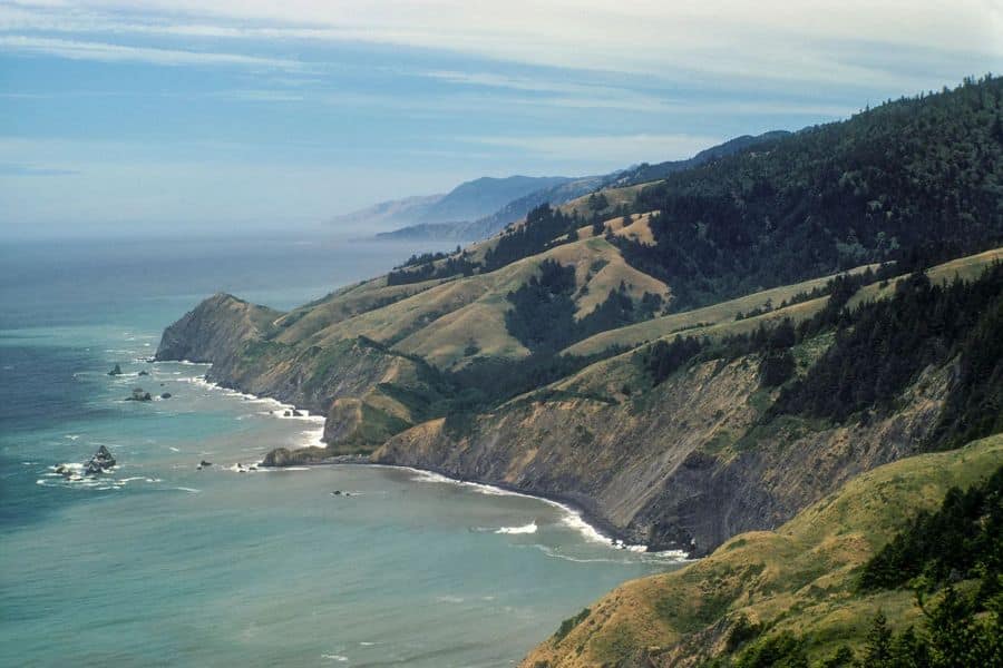 A hazy view of the rugged Lost Coast in Northern California, where steep cliffs meet wild ocean. Remote and untamed, it’s one of the most challenging coastal hiking trails in the US.