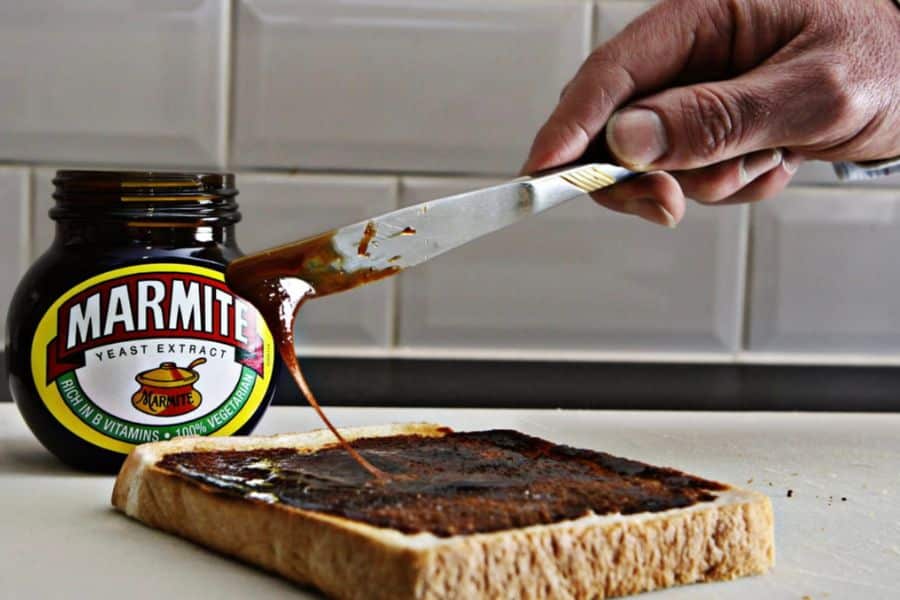 A hand spreading Marmite on a slice of bread with a jar labeled "yeast extract" in the background. Marmite is rich in B vitamins, supporting brain health and making it one of the superfoods that help slow the aging process.