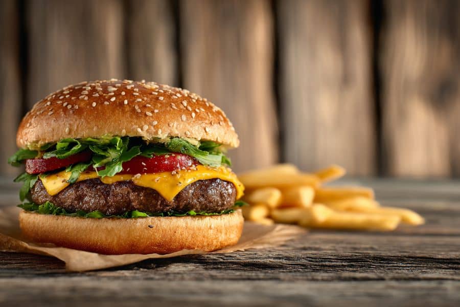 Juicy cheeseburger with fries on a rustic wooden surface, a classic example of fast food among the 9 common foods to avoid.