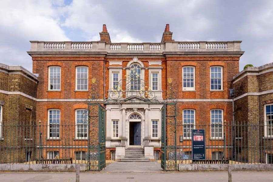 Exterior of a Georgian-style red-brick mansion with ornate wrought iron gates and stone steps leading to the entrance. As one of the Bridgerton locations, this house adds authenticity to the show's historical setting.