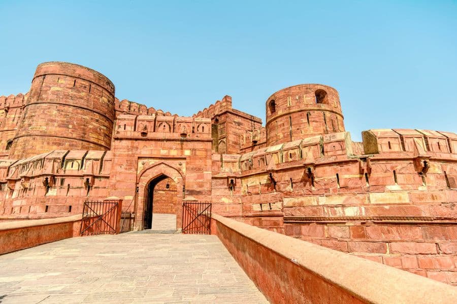 The massive red sandstone walls of Agra Fort in India stand under a clear blue sky. Rich in Mughal architecture and history, it’s one of the cultural Bucket List Destinations to Visit.