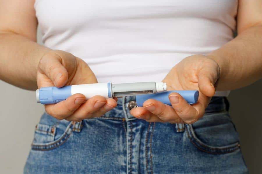 Close-up of a person holding an insulin pen, representing medical conditions like diabetes that can be part of The Weight Loss Trap.
