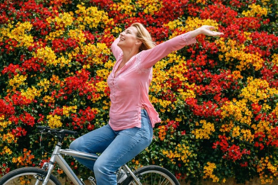 Woman in jeans and a pink top riding a bike past lots of yellow and red flowers