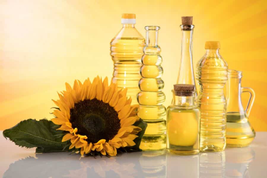 Assorted bottles of yellow sunflower oil arranged in a row beside a fresh sunflower, representing seed oils often included in the list of 9 common foods to avoid.