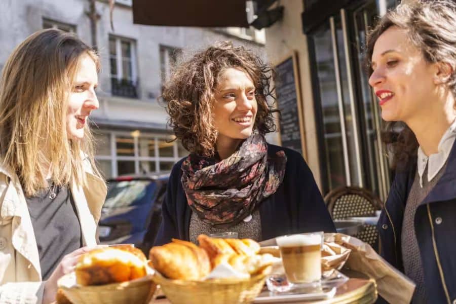 Three women sitting at a table with coffee and pastries