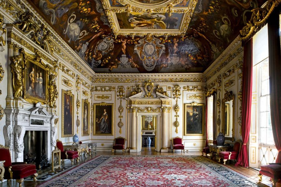 Ornate palace interior with gilded walls, dramatic ceiling frescoes, royal red drapes, and classical portraits. This lavish space is one of the Bridgerton locations used to depict the luxurious settings of high-society life.