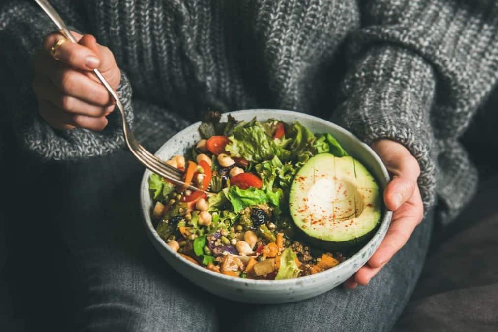 Bowl of hearty salad with chickpeas leafy greens grains and half an avocado showing plant foods that build muscle in a balanced meal.
