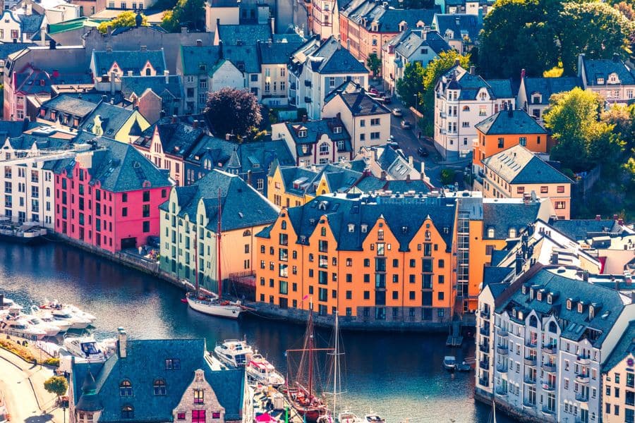 Most Colorful Places in Europe showcasing a harbor town with rows of pastel and bold painted buildings in orange, blue, and pink clustered along the waterfront. Sailboats rest in the marina below, emphasizing the striking contrast between the colorful architecture and deep blue water.