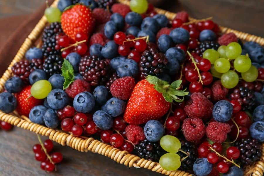 A woven basket overflowing with strawberries, blueberries, blackberries, raspberries, red currants, and green grapes. Berries are packed with antioxidants and polyphenols, making them powerful foods that can reverse aging and fight inflammation.