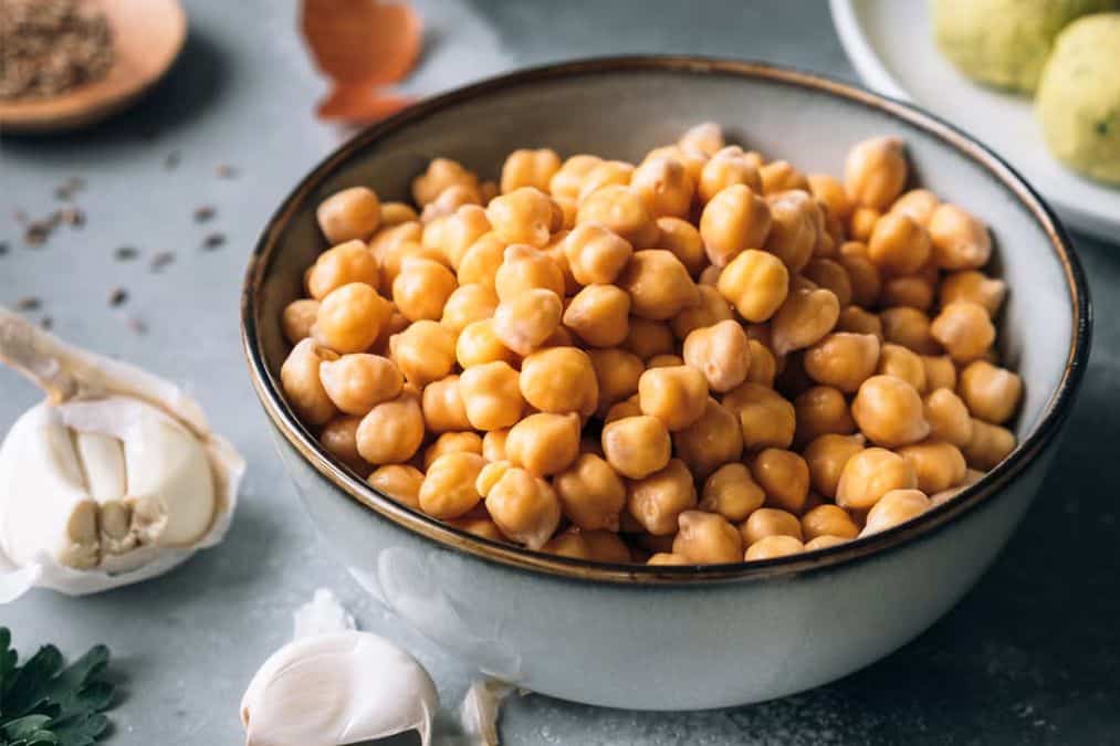 Close up of cooked chickpeas in a bowl with garlic nearby highlighting plant foods that build muscle.