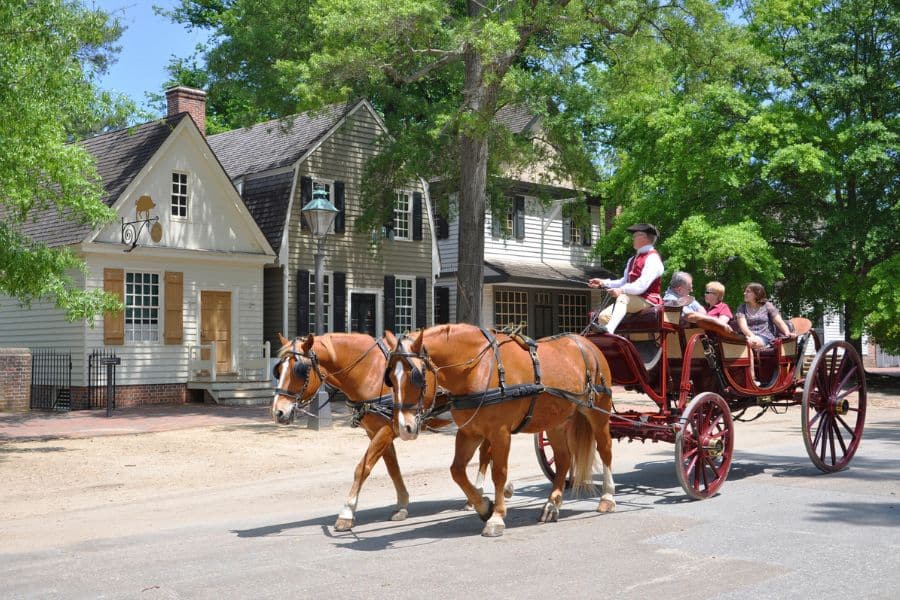 Horse drawn carriage carrying visitors past colonial style buildings and shaded streets in historic American towns.
