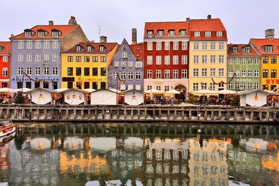 A vibrant row of historic buildings painted in bright colors lines the Nyhavn canal, with reflections in the water and open-air cafés buzzing with people. Copenhagen’s compact layout and waterfront charm make it one of the most walkable cities in Europe.
