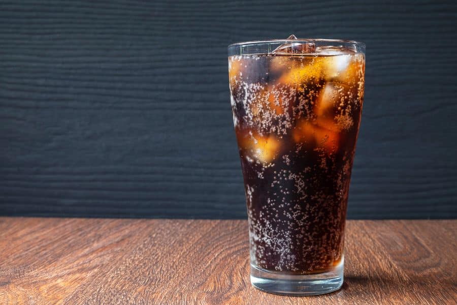 Glass of dark soda filled with ice and bubbles on a wooden surface showing sugary drinks as Foods Aging Your Brain.