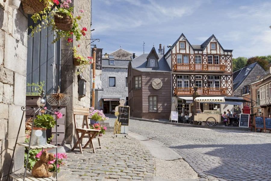 A cobblestone street lined with flowers and timber-framed houses leads to a cozy café in the medieval village of Monschau, Germany. This picturesque corner highlights the warmth and character found in many historic villages in Europe.