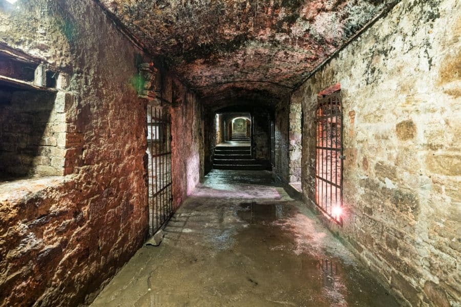 Rough white stone chamber with carved doorways and exposed rock textures, demonstrating the hand hewn rooms typical of Underground Cities in Europe. Warm lighting from within the passageways draws attention to the depth of the carved interior.