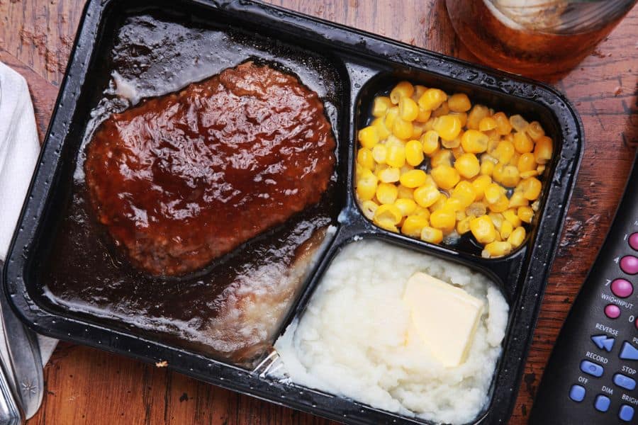 Frozen TV dinner with meat patty mashed potatoes and corn in a plastic tray symbolizing highly processed Foods Aging Your Brain.