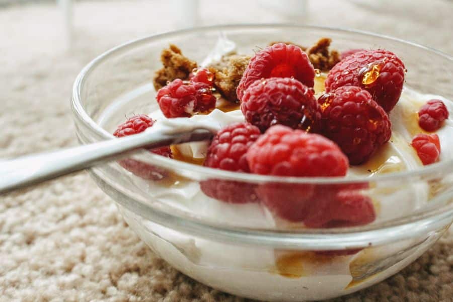 A clear bowl of creamy yogurt topped with fresh raspberries, a drizzle of honey, and crunchy granola sits beside a spoon. This probiotic-rich snack is a gut-friendly choice among foods that can reverse aging and support immune health.