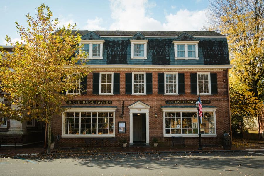 Traditional brick tavern with dormer windows and fall foliage framing the facade in historic American towns.