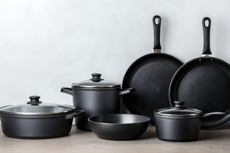 Set of black nonstick pots and pans with lids displayed on a countertop. The cookware suggests concerns about harmful toxins that can be released from certain nonstick coatings at high temperatures.