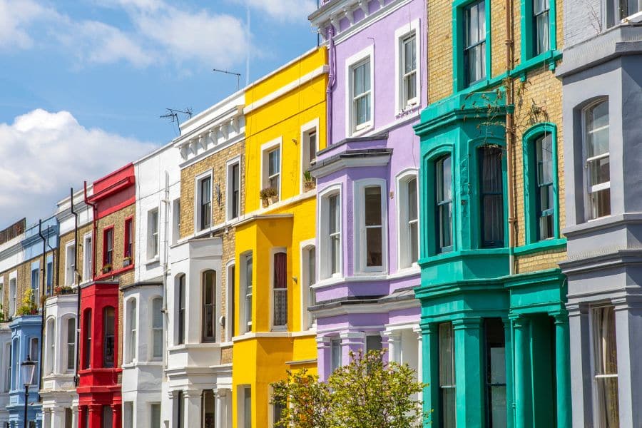 Most Colorful Places in Europe featuring a row of terraced houses painted in bold shades of red, yellow, purple, and teal along a sunny residential street. The bright facades stand side by side, creating a vibrant and playful urban scene.