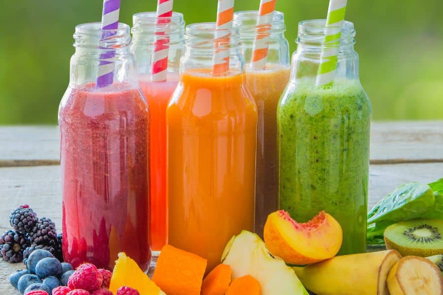 Colorful bottled smoothies made from berries, mango, kiwi, and leafy greens with striped straws. Store bought smoothies can become Breakfast Staples Triggering Inflammation if they are high in added sugars and low in fiber.