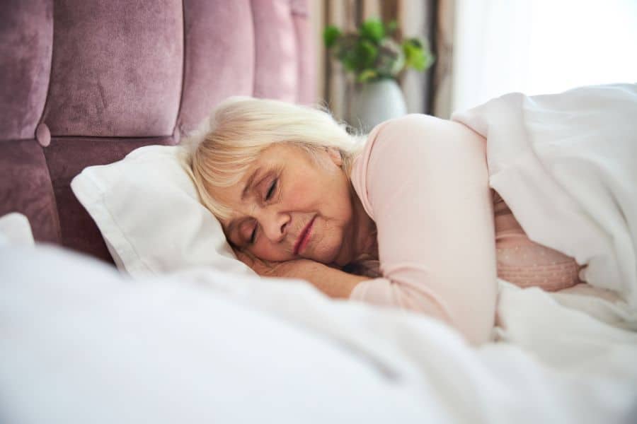 Older woman sleeping peacefully on her side in a softly lit bedroom, illustrating the importance of rest for Weight Loss In Midlife. The calm setting and relaxed expression reinforce healthy sleep habits as part of overall wellness.