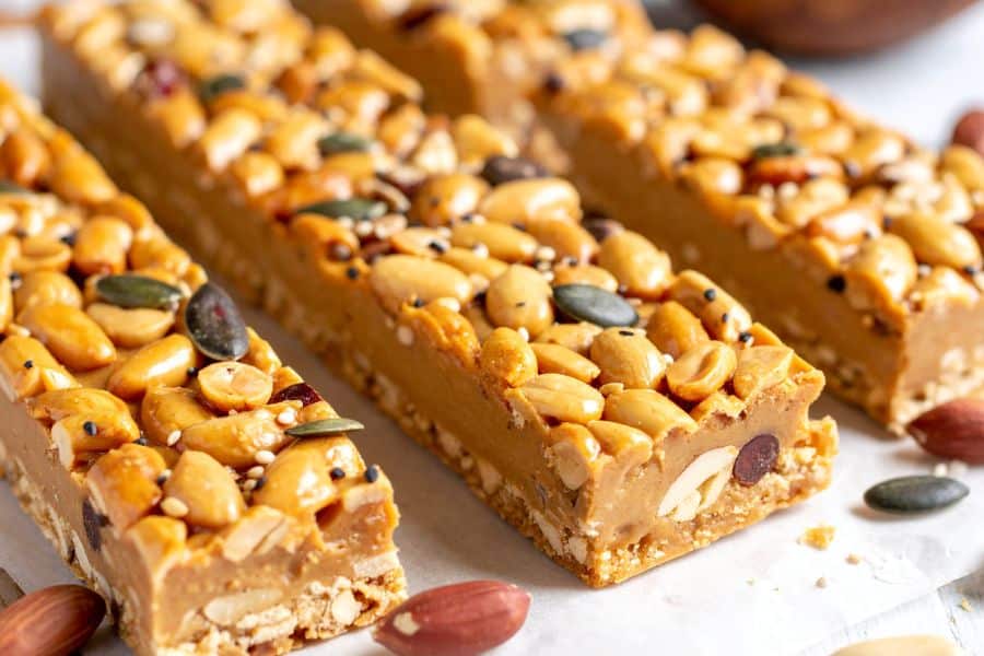 Close up of nut and seed bars topped with peanuts, pumpkin seeds, sesame seeds, and almonds. Processed granola or snack bars like these may be Breakfast Staples Triggering Inflammation when they include syrups and added sugars.
