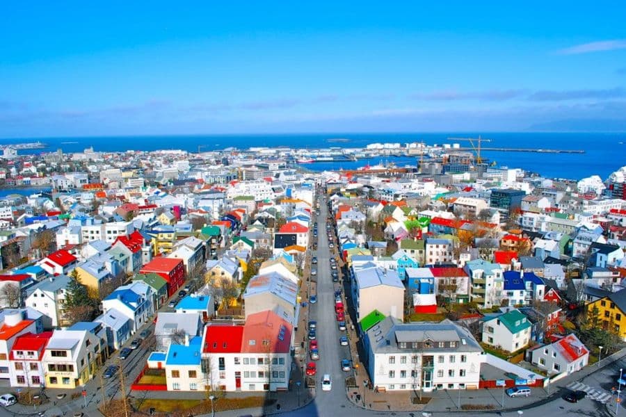 Most Colorful Places in Europe overlooking a coastal city filled with rooftops painted in red, blue, green, and white stretching toward the sea. The aerial view emphasizes the patchwork of colorful homes against the deep blue ocean horizon.