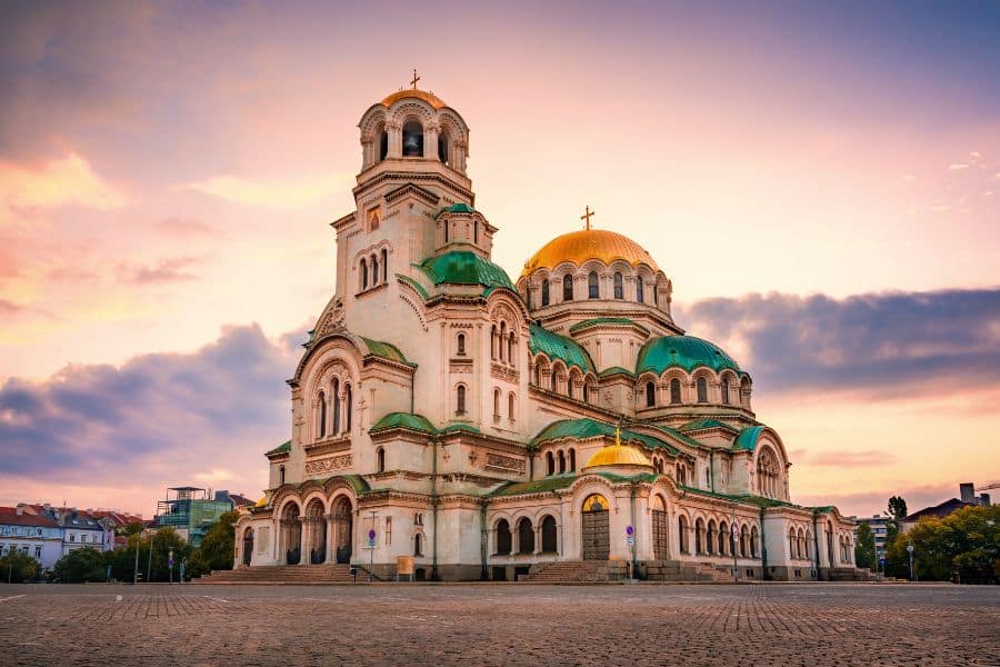 A grand cathedral with golden domes glowing at sunset, illustrating the architectural splendor found in many European capital cities. The wide open square emphasizes the scale and symmetry of the landmark.
