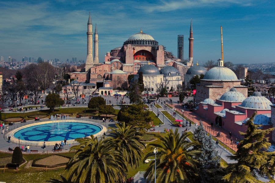 A panoramic view of a monumental mosque and surrounding domes rising above a bustling square, highlighting the rich cultural layers within European capital cities. Palm trees and historic structures frame the skyline.