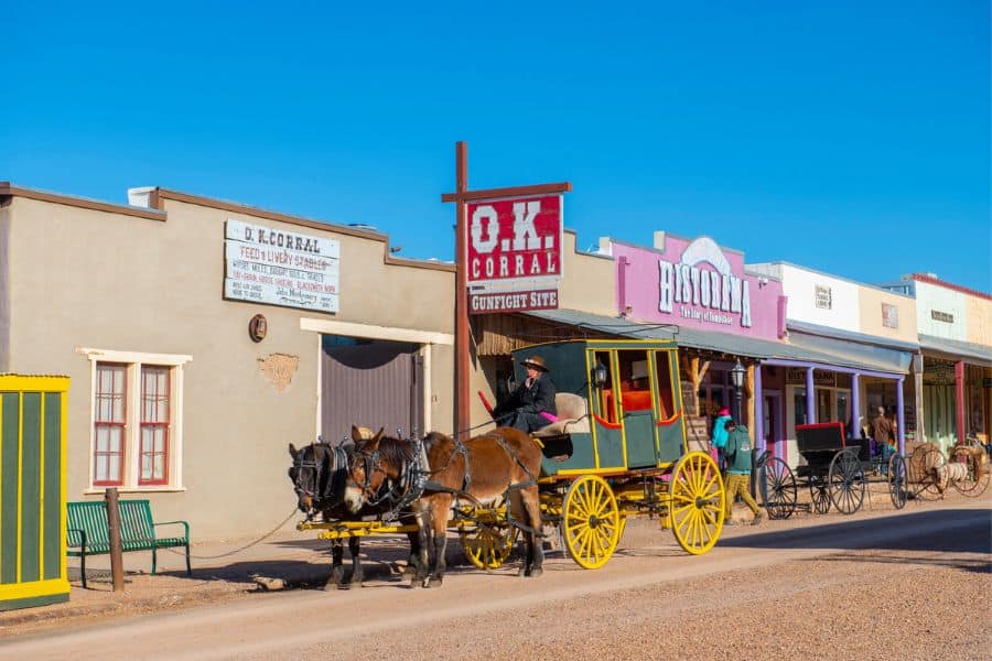 Stagecoach parked outside old western storefronts including the OK Corral sign in historic American towns.