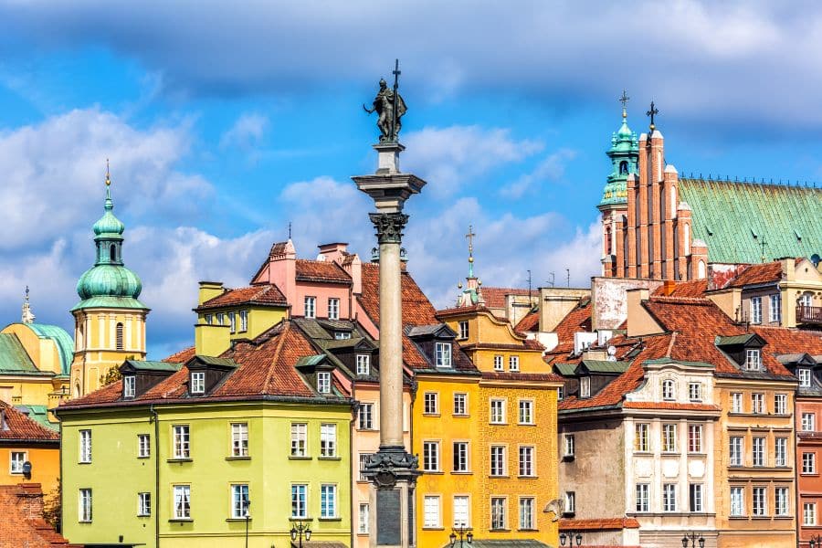 Vibrant townhouses in shades of green, yellow, and orange stand beside Sigismund's Column under a blue sky in Warsaw’s UNESCO-listed Old Town. With its restored charm and pedestrian-friendly streets, Warsaw deserves a spot among the most culturally rich walkable cities in Europe.