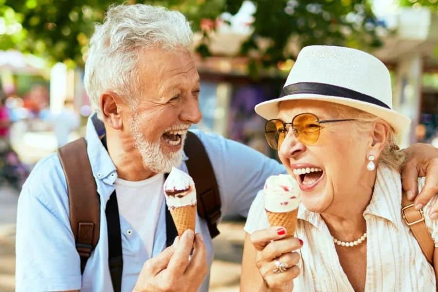 An older couple laugh together outdoors while holding ice cream cones on a sunny day. Sharing joyful moments and time outside can support brain-boosting habits that help keep daily life social and engaging.