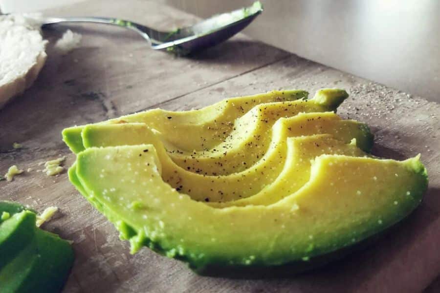 Sliced avocado fanned out on a wooden cutting board with coarse salt and black pepper sprinkled on top. This close up supports content about foods that may help lower your cholesterol by showing fresh avocado ready to eat.