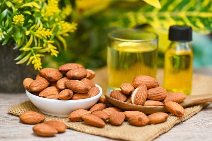 Bowl and wooden spoon filled with whole almonds sit beside a small bottle and glass of golden almond oil on a woven mat. This close up works well for calcium rich foods because it highlights almonds as a nutrient dense snack and ingredient.