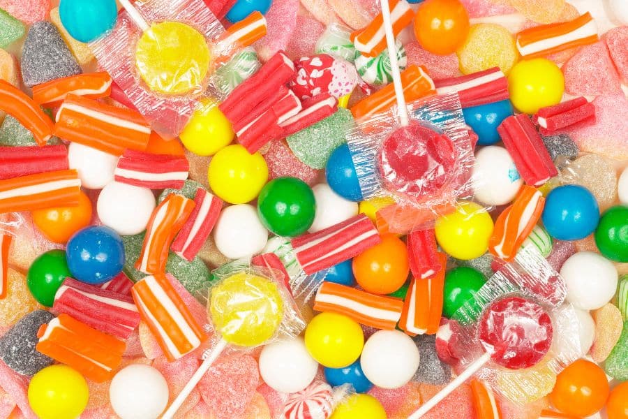 Bright assortment of candy spread across a white background with lollipops gumdrops striped chews and round gumballs. The mix of sugary sweets suggests foods that can quickly satisfy cravings.