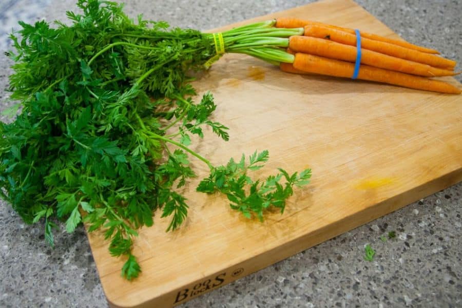 Bunch of carrots with bright green tops rests on a large wooden cutting board. This photo suits a piece about edible leaves because it shows carrot greens still attached and ready for kitchen use.