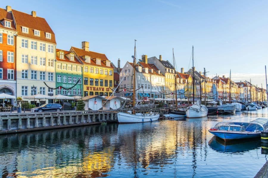 Colorful waterfront buildings line a calm canal filled with sailboats and small boats moored along the edge. This lively harbor scene shows why Copenhagen is often featured among retiree hotspots in Europe.