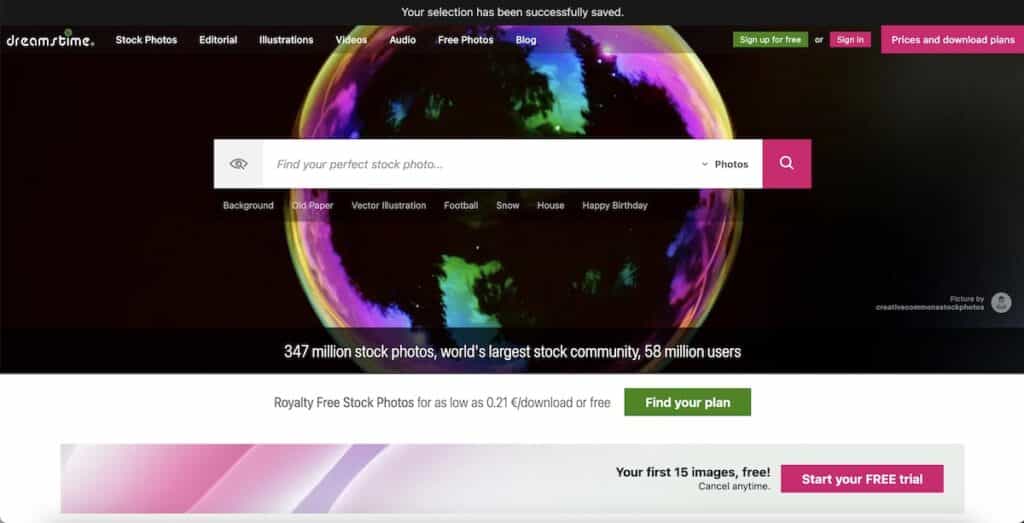 Screenshot of the Dreamstime homepage with a dark banner showing a large rainbow colored bubble behind the search bar. Visible text includes "Your selection has been successfully saved." "dreamstime" "Stock Photos" "Editorial" "Illustrations" "Videos" "Audio" "Free Photos" "Blog" "Sign up for free" "Sign in" "Prices and download plans" "Find your perfect stock photo..." "Photos" "Background" "Old Paper" "Vector Illustration" "Football" "Snow" "House" "Happy Birthday" "Picture by creativecommonsstockphotos" "347 million stock photos, world's largest stock community, 58 million users" "Royalty Free Stock Photos for as low as 0.21 € download or free" "Find your plan" "Your first 15 images, free." "Cancel anytime." and "Start your FREE trial."