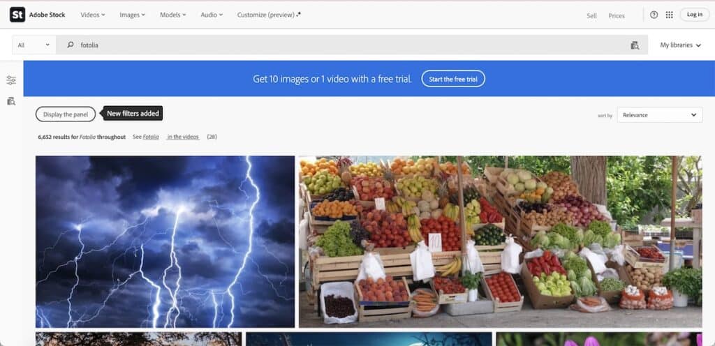 Screenshot of Adobe Stock search results for Fotolia with a blue free trial banner across the top and large thumbnails of lightning and a fruit stand below. Visible text includes "Adobe Stock" "Videos" "Images" "Models" "Audio" "Customize preview" "Sell" "Prices" "Log in" "fotolia" "My libraries" "Get 10 images or 1 video with a free trial." "Start the free trial" "Display the panel" "New filters added" "6,652 results for Fotolia throughout" "See Fotolia" "in the videos" and "sort by Relevance."