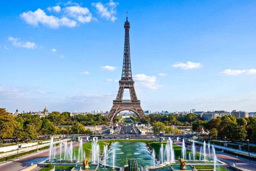 The Eiffel Tower rises over Paris under a bright blue sky with fountains spraying in the foreground and tree lined avenues leading toward the landmark. Paris is shown here as one of the most iconic urban retiree hotspots in Europe.
