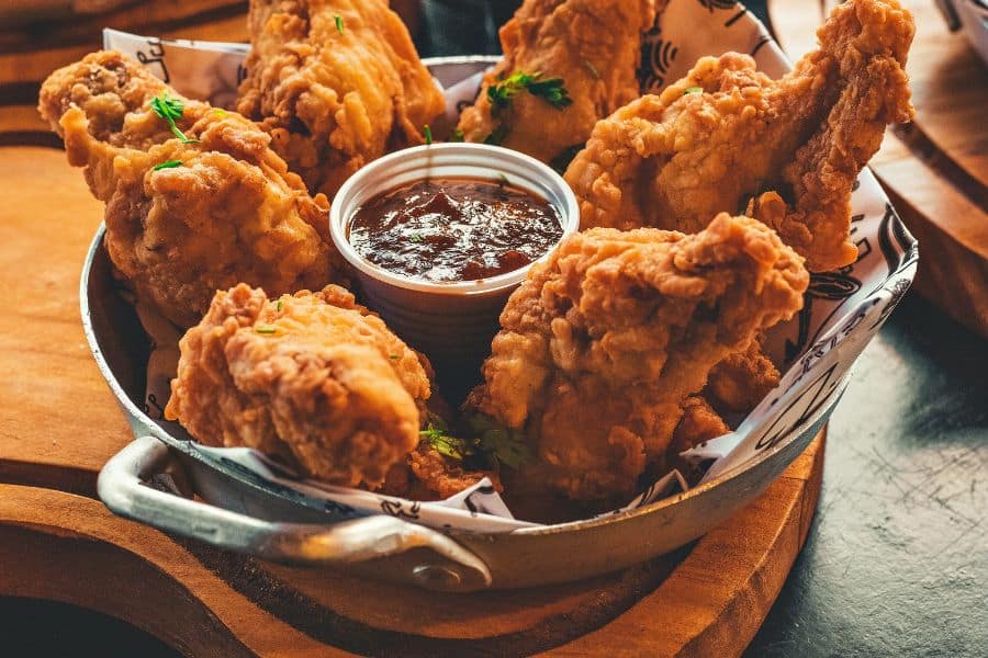 Basket of crispy fried chicken pieces arranged around a small cup of dark dipping sauce. The golden breading and rich texture make this look like a heavy comfort food meal.