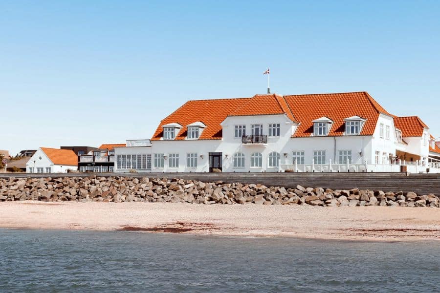 Seaside hotel with red tiled roof facing calm blue water along the coast near European National Parks.