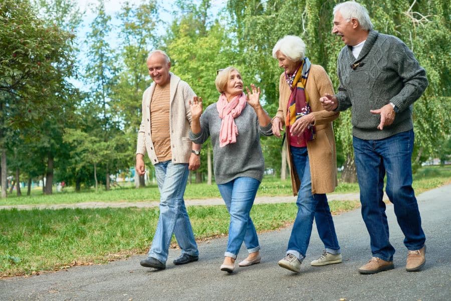 Four older adults walk together on a paved path through a green park while chatting and smiling. Walking with friends combines movement and social connection, two brain-boosting habits that can support cognitive health.