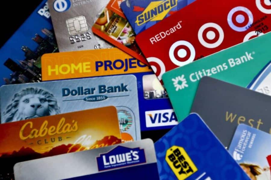 Close up of overlapping credit and store cards from different brands arranged in a pile. The stacked cards reinforce themes of debt, borrowing, and consumer spending during inflation.