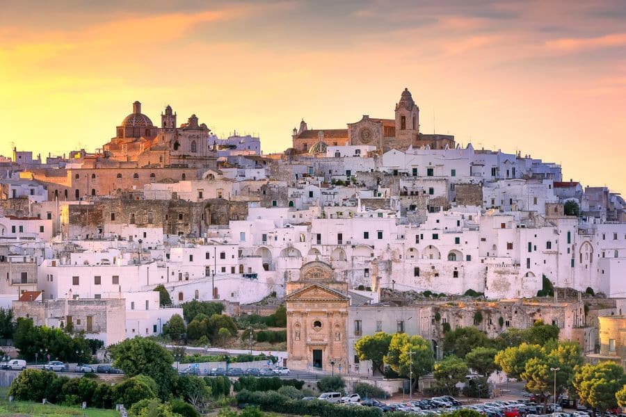 Whitewashed buildings and cathedral domes glowing at sunset in a historic town center highlighting picturesque villages in Italy.