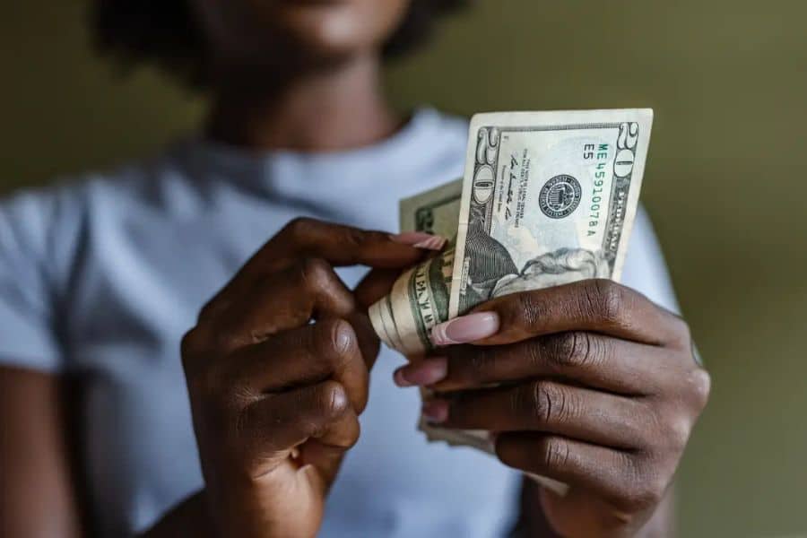 Close up of hands counting a small stack of US dollar bills against a dark blurred background. The tight crop emphasizes stretching cash to make it through the week.