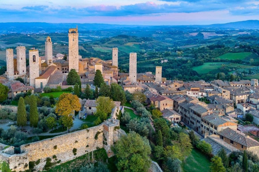 Hilltop town with tall medieval towers surrounded by rolling green countryside representing iconic villages in Italy.