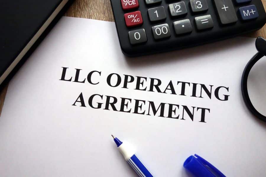 Close up of a document labeled "LLC OPERATING AGREEMENT" with a calculator pen and eyeglasses placed around it. The image highlights paperwork and financial tools that may be part of retirement and business planning.