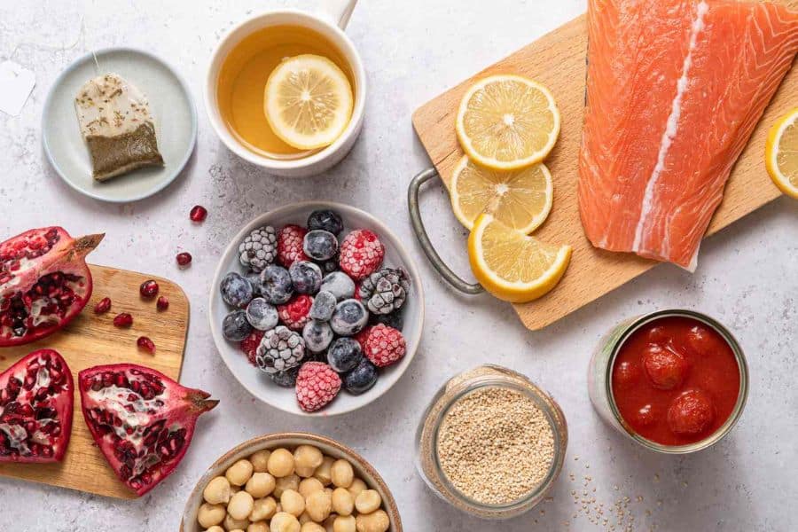 Overhead view of anti inflammatory foods arranged on a table including salmon lemon tea berries pomegranate quinoa chickpeas and tomatoes. This sciatica related wellness photo suggests foods commonly associated with reducing inflammation.